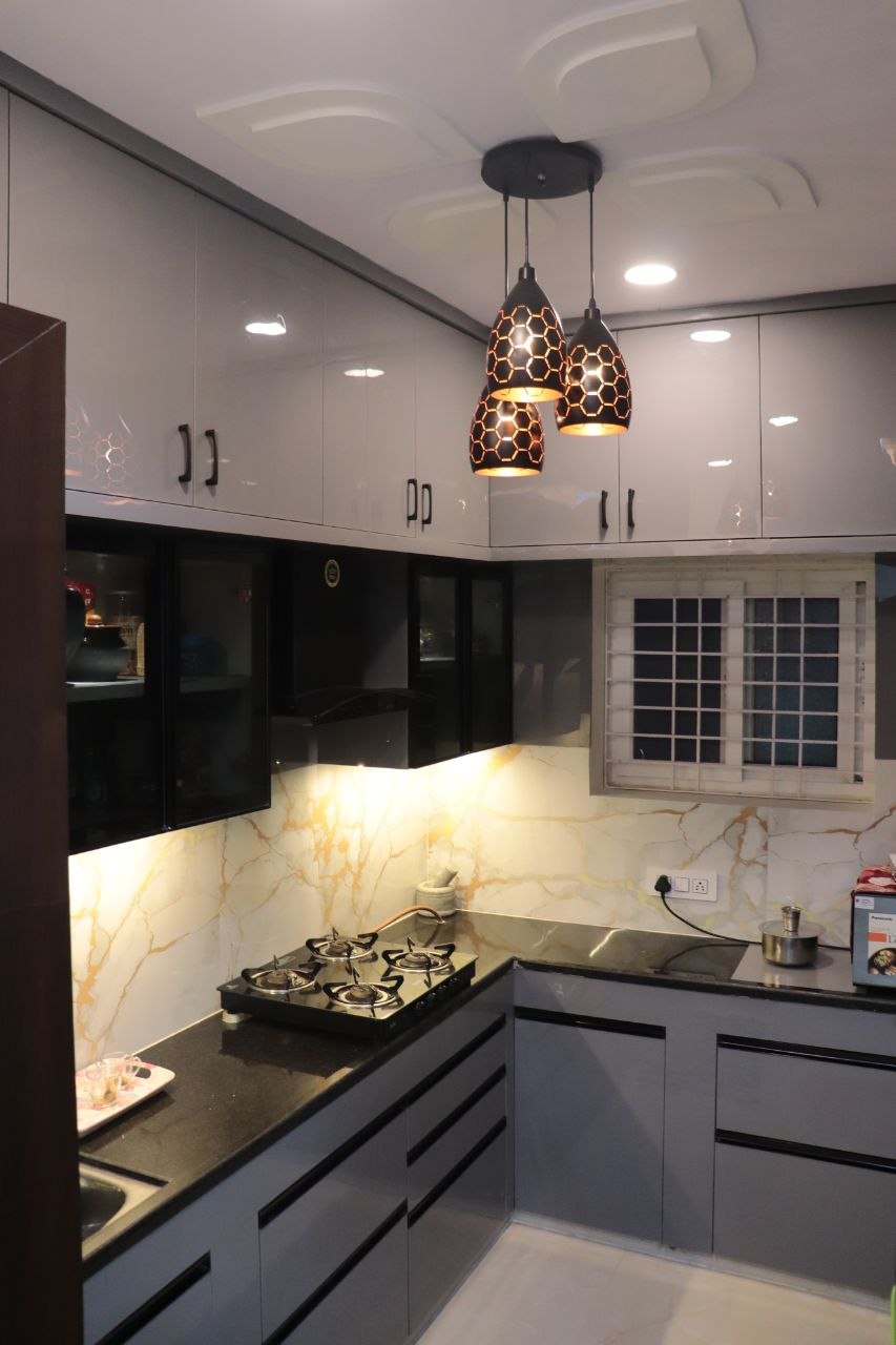 Grey and black modular kitchen with gold-veined marble backsplash and honeycomb pendant lights — by Vinterior Hub, Hyderabad
