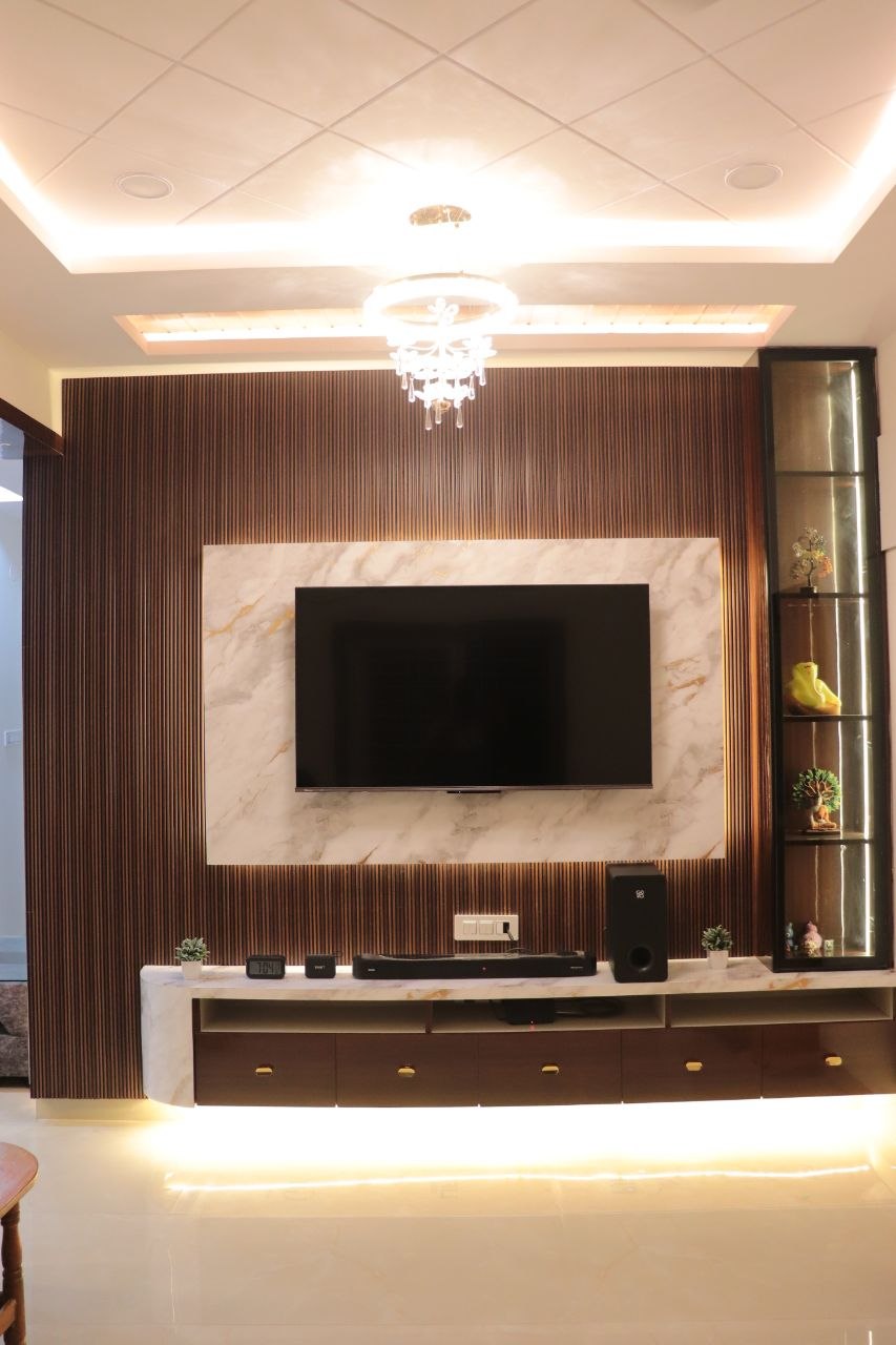 Fluted walnut-veneer TV wall with marble panel and cove lighting — apartment living-room interior by Vinterior Hub, Hyderabad